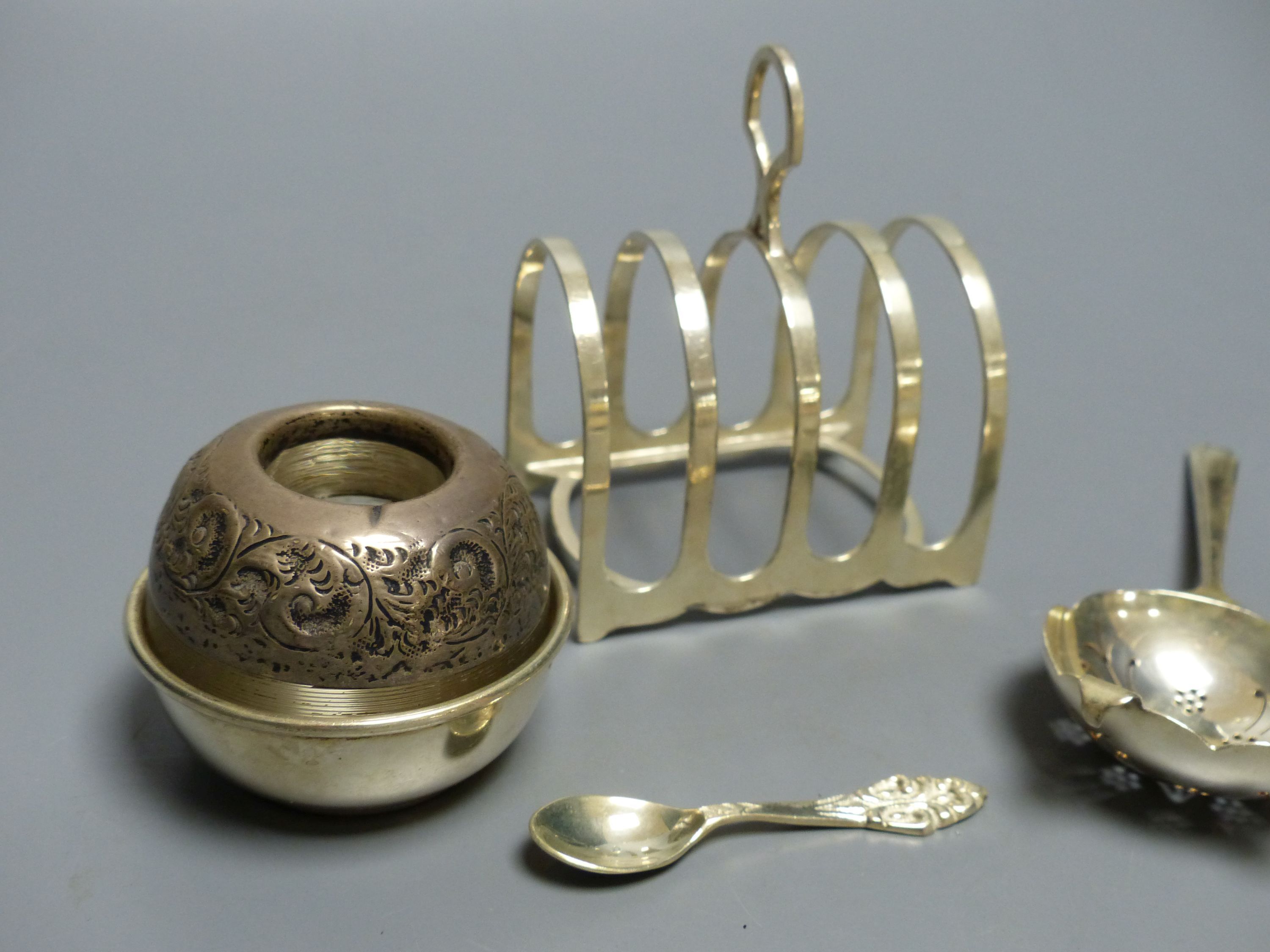 A silver tea strainer, Sheffield, 1964, a George V silver toast rack and an early 20th century silver mounted match tidy,